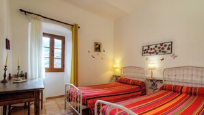 Ein Schlafzimmer mit zwei Betten, einem Holztisch, einem Fenster mit Vorhängen, Wanddekorationen und Nachttischlampen.