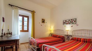 A bedroom with two beds, a wooden desk, a window with curtains, wall decorations, and bedside lamps. - Anne-Lise - AVAPESSA (AVAPESSA)