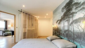 A bedroom with a bed, a painting of trees, a curtain, and a sofa in the adjacent room. - 2Calm - VIGGIANELLO - Gîte (VIGGIANELLO)