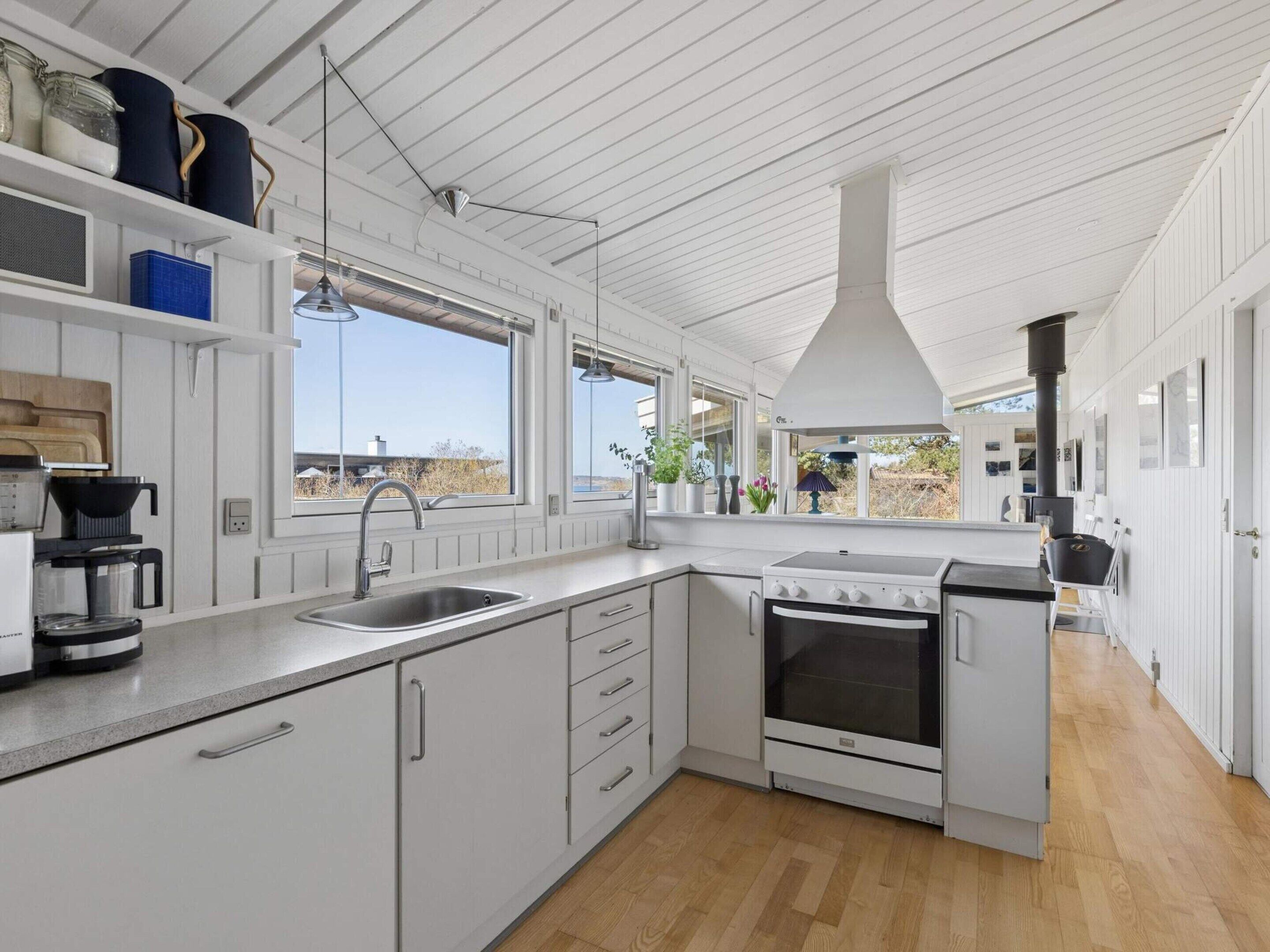 A modern kitchen with white cabinetry, a built-in oven, a sink, and a large window offering a view of the outdoors.