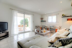 Ein Wohnzimmer mit Flachbildfernseher, einer Couch, einem Esstisch mit Stühlen und einer Glastür zum Außenbereich.