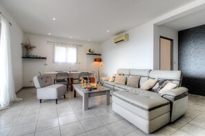 Ein modernes Wohnzimmer mit einer Couch, Sesseln, einem Couchtisch und einem Essbereich mit Tisch und Stühlen.