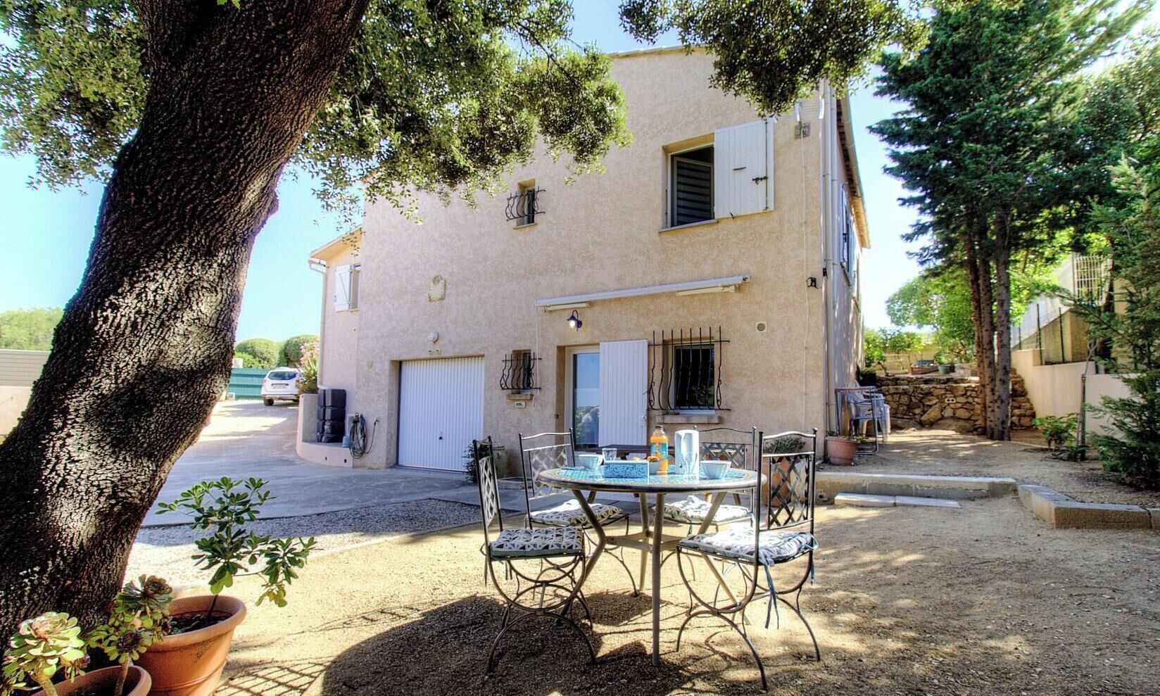 Edifici amb garatge, un pati amb taula i cadires i plantes en testos.
