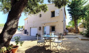 Ein Gebäude mit Garage, einer Terrasse mit Tisch und Stühlen sowie Pflanzkübeln.
