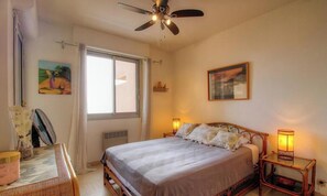 Ein Schlafzimmer mit Bett, Nachttischlampen, Deckenventilator, Fenster und einem Bild an der Wand.