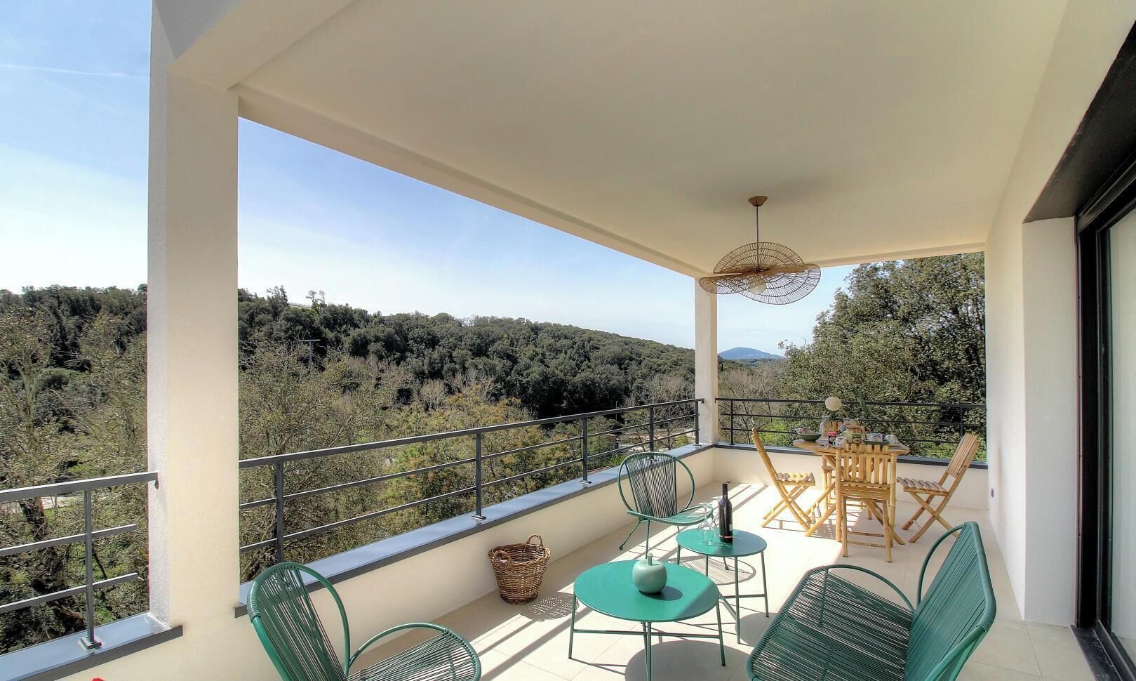 Ein Balkon mit Gartenmöbeln, einem Korbwäsche und Blick auf einen bewaldeten Hang.
