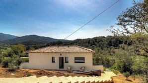 Une maison de plain-pied avec un toit en tuiles, un petit porche et une vue sur un paysage vallonné.
