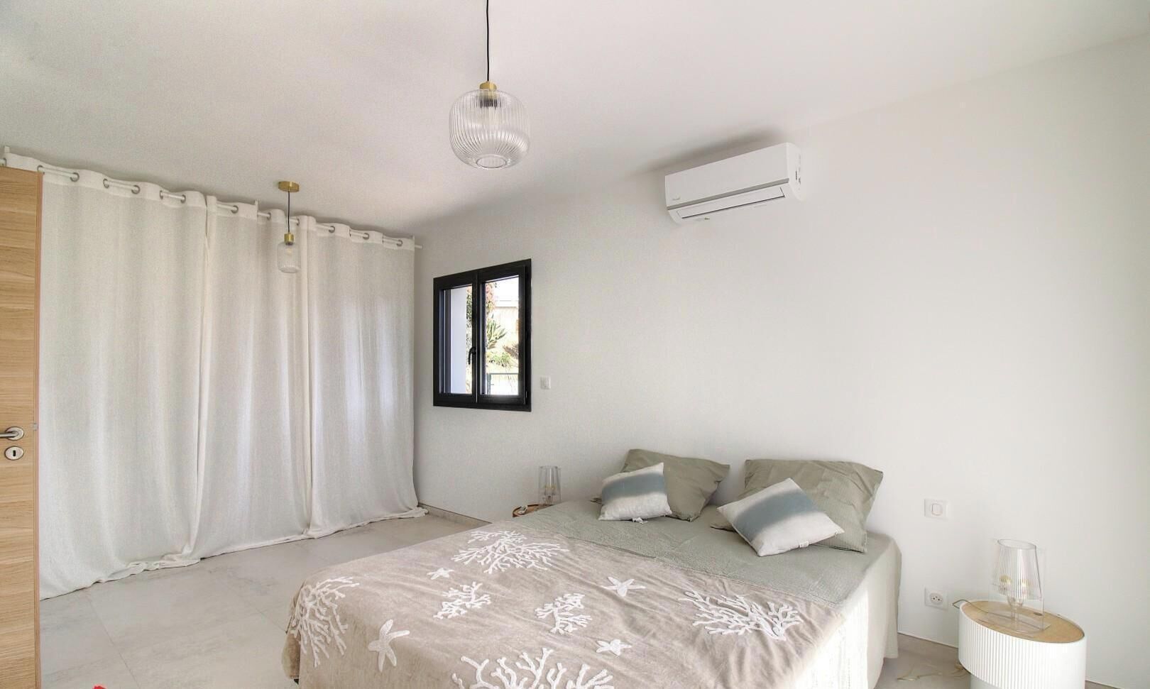 Ein Schlafzimmer mit Bett, Vorhängen, einem Fenster, einer Klimaanlage und einem Nachttisch.
