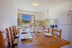 Ein Esszimmer mit Holztisch, gedeckt für sechs Personen, Küchengeräten und einem Fenster mit Blick.