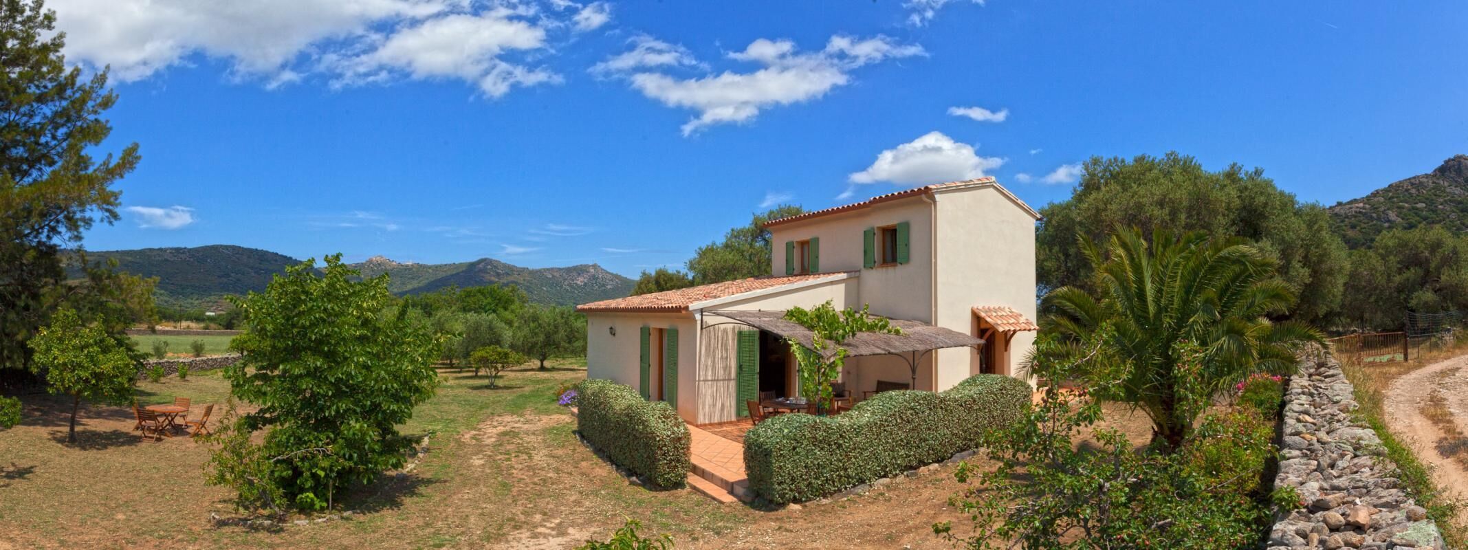A single-story house with a patio, surrounded by trees and mountains.