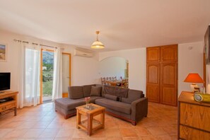 Ein Wohnzimmer mit einer Couch, einem Couchtisch, einem Fernseher und einem Essbereich, der durch eine Glastür sichtbar ist.