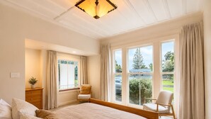Ein Schlafzimmer mit einem großen Bett, zwei Stühlen, einem Schminktisch und einem Fenster mit Vorhängen.