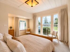 Ein Schlafzimmer mit einem großen Bett, zwei Stühlen, einem Schminktisch und einem Fenster mit Vorhängen.