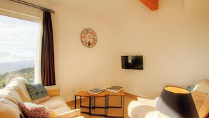 Ett mysigt vardagsrum med en soffa, ett soffbord med böcker, en väggklocka, en platt-TV och ett fönster med gardiner.