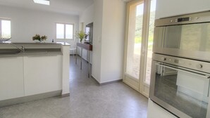 Une cuisine moderne dotée d’un îlot central, d’un four encastré et d’une porte-fenêtre coulissante donnant sur un patio.