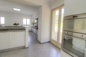 A modern kitchen with a central island, built-in oven, and a sliding glass door leading to a patio. - Casa di Catalina è Batistina (SOLLACARO)