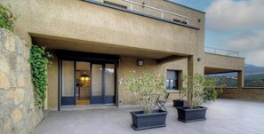 Un edificio moderno con un muro de piedra, una entrada de vidrio y plantas en macetas en el patio.