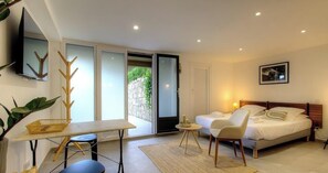 Un dormitorio con cama, escritorio, silla, televisión y puerta corrediza de vidrio que da a un balcón.