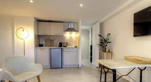 Una cocina moderna con armarios blancos, horno empotrado y comedor con mesa y silla.