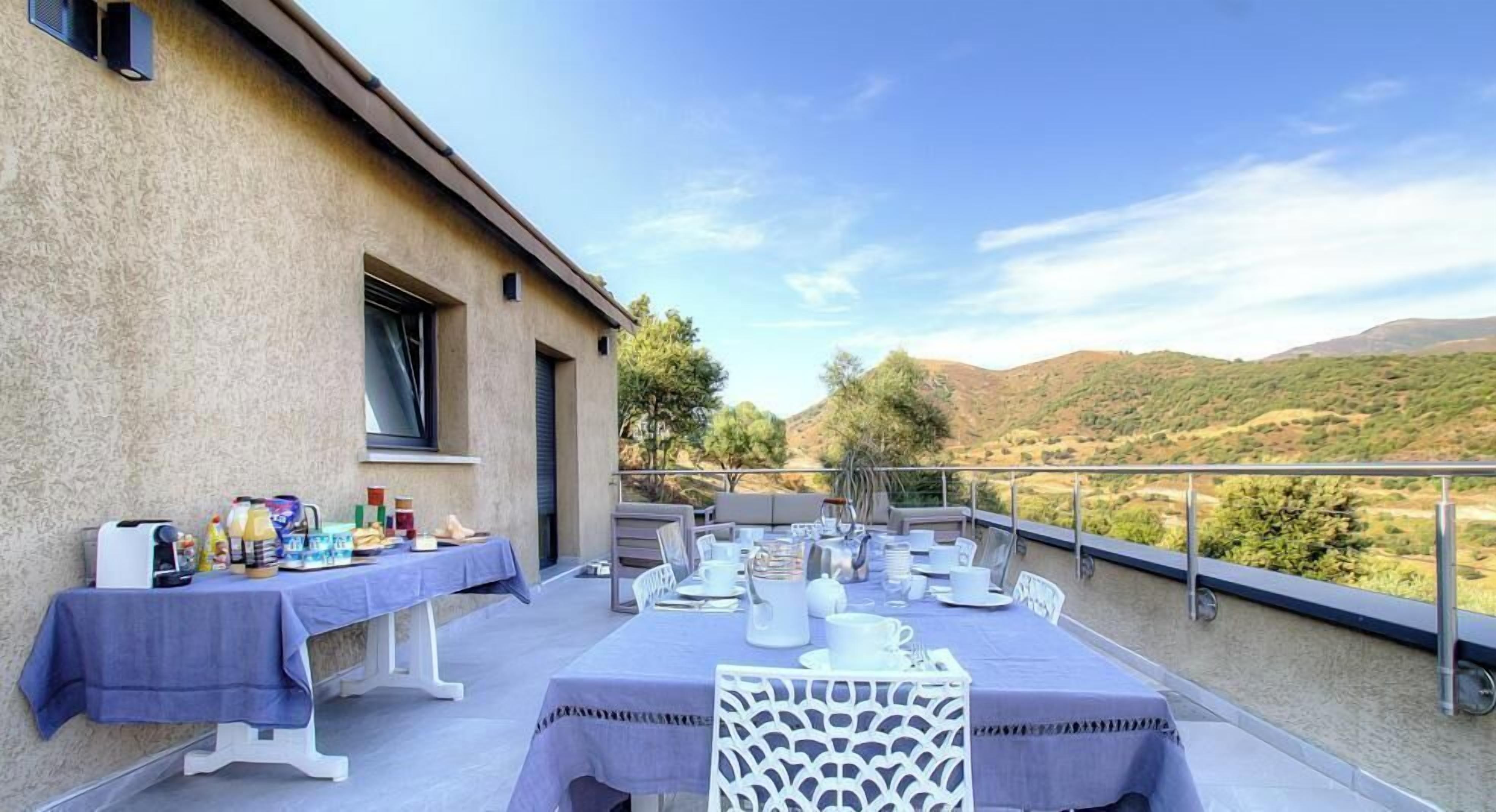 Un espace extérieur aménagé pour les repas, avec des tables dressées, offrant une vue sur un paysage vallonné.