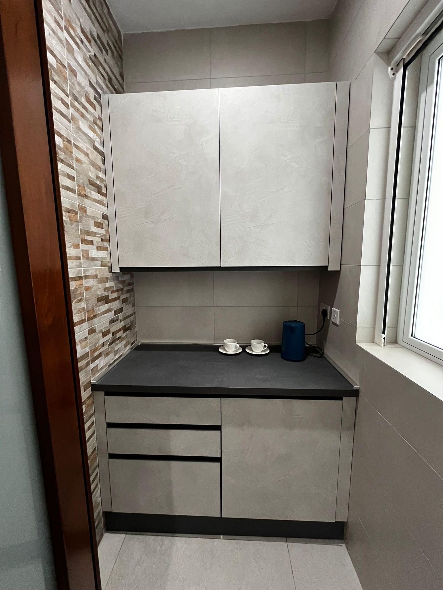 A compact kitchen with a black countertop, two white cups, and a blue container.