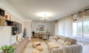 Un saló amb un sofà, una televisió, una làmpada de cristall i una zona de menjador.