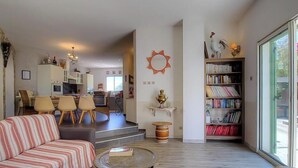Una sala de estar con sofá, una mesa de centro, una estantería y una zona de comedor con sillas y una mesa.