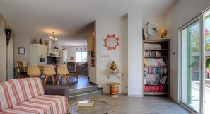 A living room with a sofa, a coffee table, a bookshelf, and a dining area with chairs and a table. - A casa sopra - TALASANI (TALASANI)