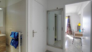 Ein Zimmer mit weißer Tür, einem Spiegel, einem Holzschrank und einem Tisch mit Stühlen.