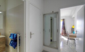 Ein Zimmer mit weißer Tür, einem Spiegel, einem Holzschrank und einem Tisch mit Stühlen.