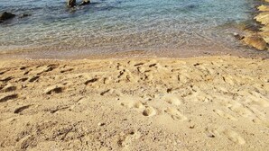 Ein sandiger Strand mit klarem Wasser und Felsformationen.
