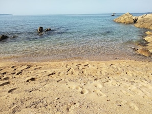 Ein sandiger Strand mit klarem Wasser und Felsformationen.