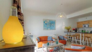 Ein modernes Wohnzimmer mit einem großen, orangefarbenen Sofa, einem Couchtisch und einer Küchenzeile mit Holzausbau und einem Barhocker.