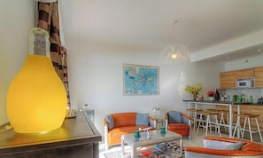 Ein modernes Wohnzimmer mit einem großen, orangefarbenen Sofa, einem Couchtisch und einer Küchenzeile mit Holzausbau und einem Barhocker.