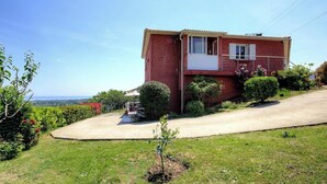 Ein rotes Backsteinhaus mit Balkon, umgeben von Grün und freiem Blick auf die Landschaft.