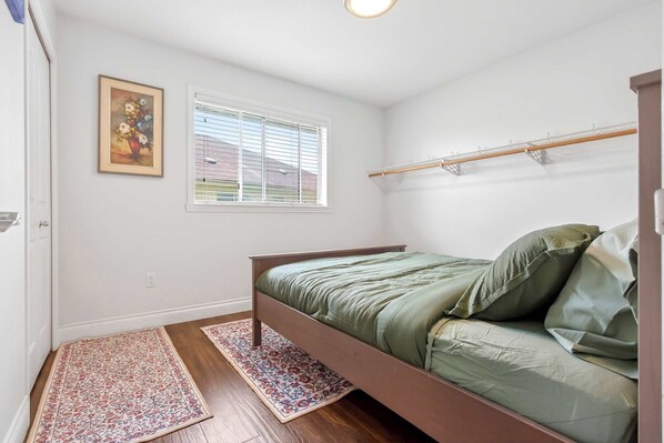Un dormitorio con una cama individual, una ventana con persianas, un estante en la pared y una puerta.