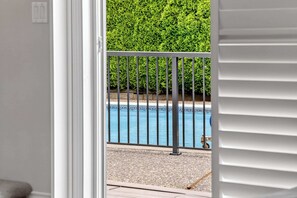 A view through a door to a swimming pool with a metal railing, surrounded by a hedge. - 2BR Surrey Pool Suite Near White Rock (Surrey)