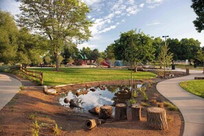 A park with a pond, wooden stumps, a playground, and a walking path. - 2BR Surrey Pool Suite Near White Rock (Surrey)