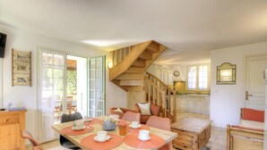 Un comedor con una escalera de madera, una cocina al fondo y una mesa de comedor con manteles individuales y tazas.