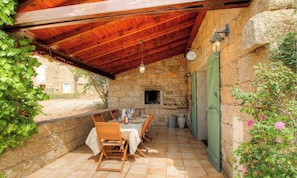 Eine Terrasse im Freien mit einer Steinwand, einem Holztisch, Stühlen, einer hängenden Leuchte und einem Steinkamin.