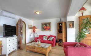 Una sala de estar con televisor, sofá rojo, mesa de centro y estantería.