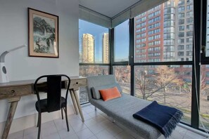 Una habitación moderna con escritorio, silla y sofá, con vistas a edificios altos.