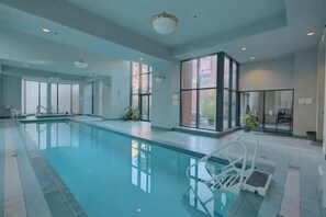 An indoor swimming pool with clear glass walls, a pool ladder, and a modern interior design.