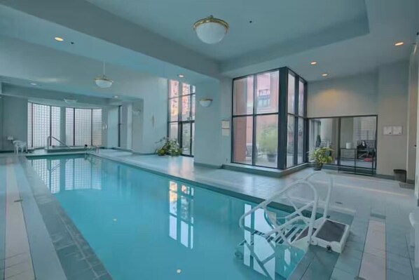 An indoor swimming pool with clear glass walls, a pool ladder, and a modern interior design.