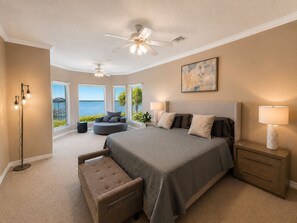 Un dormitorio con cama, una silla, una mesita de noche, una lámpara de pie y vista al mar.