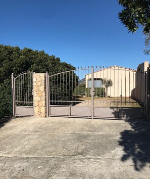 Una entrada tancada amb un pilar de pedra, una reixa de metall i un edifici amb façana color beix i una finestra.
