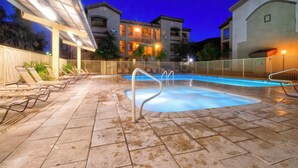 Una piscina con cubierta de baldosas, sillas de descanso y una zona techada con luces.