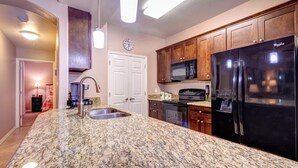 Una cocina con encimeras de granito, un refrigerador negro, un microondas y armarios de madera.