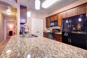 Eine Küche mit Granit-Arbeitsplatten, einem schwarzen Kühlschrank, einer Mikrowelle und Holzschränken.