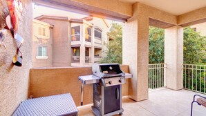 Un balcón al aire libre con una parrilla, una mesa de metal y vistas a un edificio con balcones.